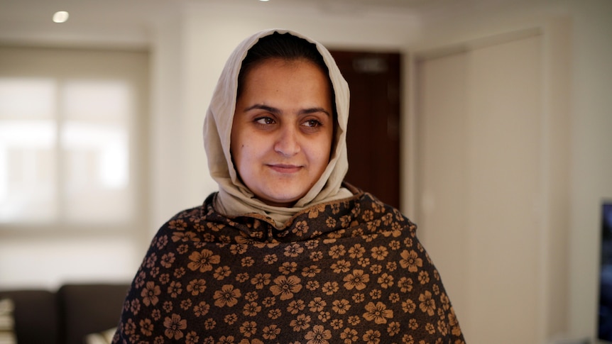 Beheshta Arghand wearing a light brown headscarf, a scarf around her and carrying an ipad.