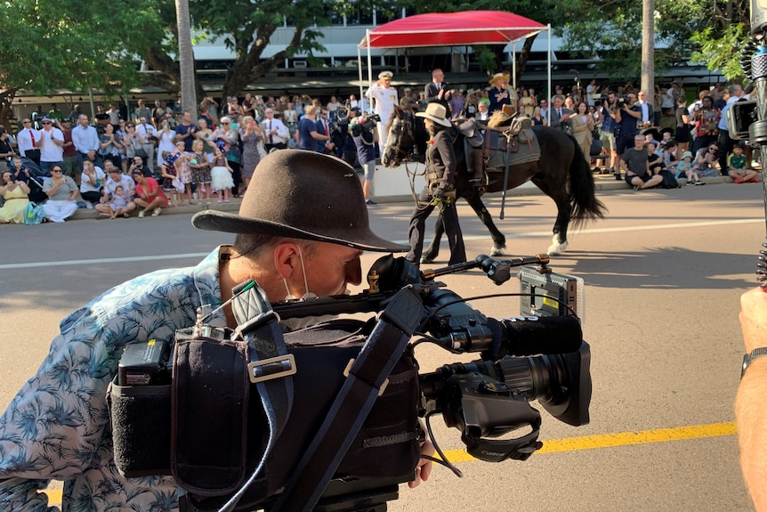 Cameraman filming parade with a woman leading a horse down the street.