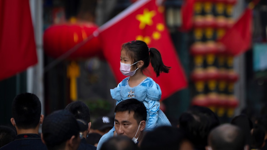 A girl wearing a face mask rides on a man's shoulders as they walk along a tourist shopping street in Beijing.