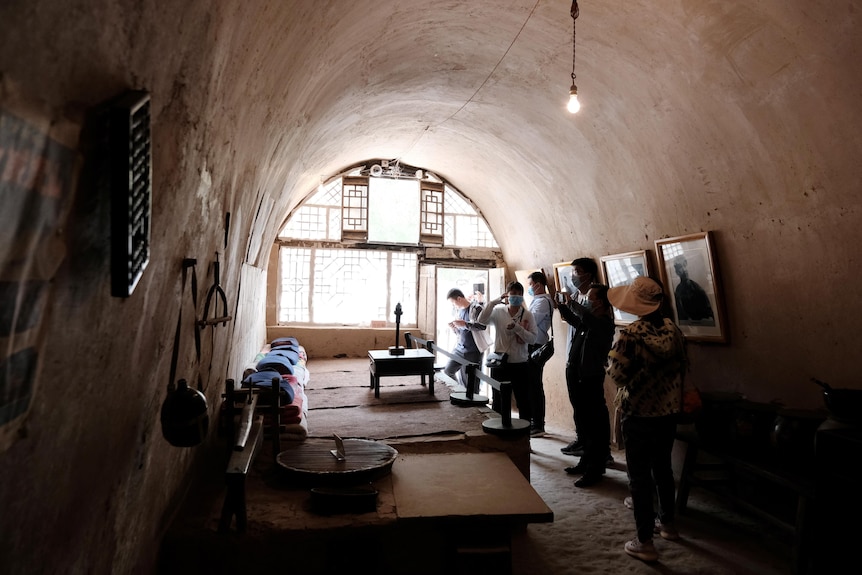 A group of people take photos in a cave-like dwelling with a bed