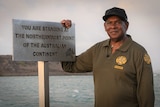 an aboriginal man stands next to the sign at the Tip of Cape York, smiling