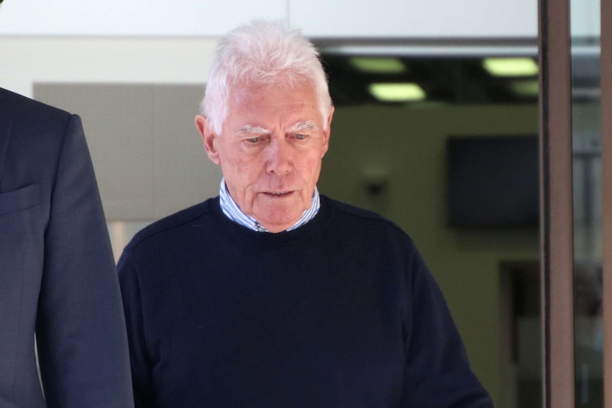 A midshot of contractor Ian Tremain walking out of a courthouse wearing a blue jumper with his head down.