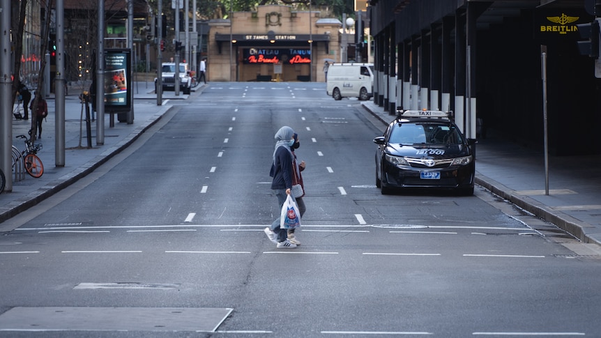Two women in headscarves stroll across an empty city street