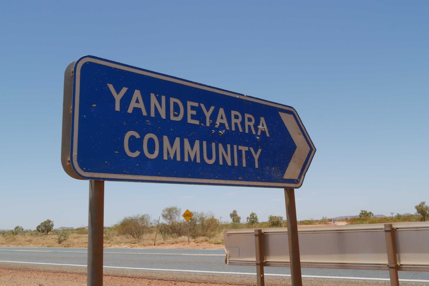 A blue road sign near an outback road points towards Yandeyarra community.