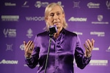Tennis great Martina Navratilova stands at a microphone clad in purple for an official tournament ceremony.