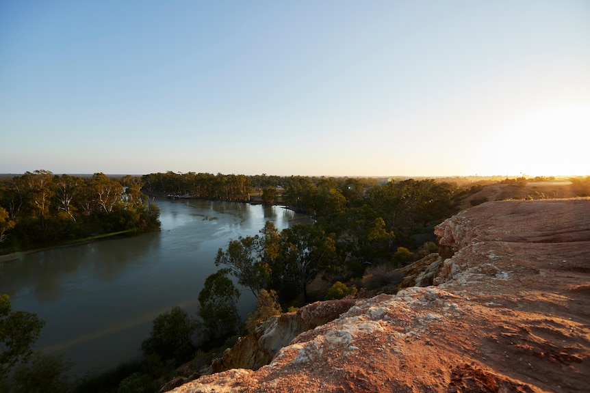 The sun shines over limestone cliffs towering above the Murray River.