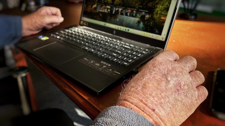 Two old man's hands resting on a computer.
