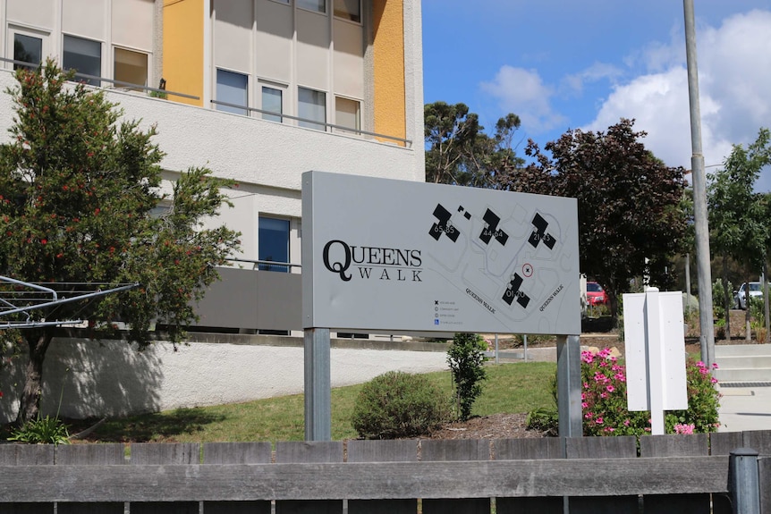 A sign reads 'Queen's Walk', with an apartment block and trees in the background.