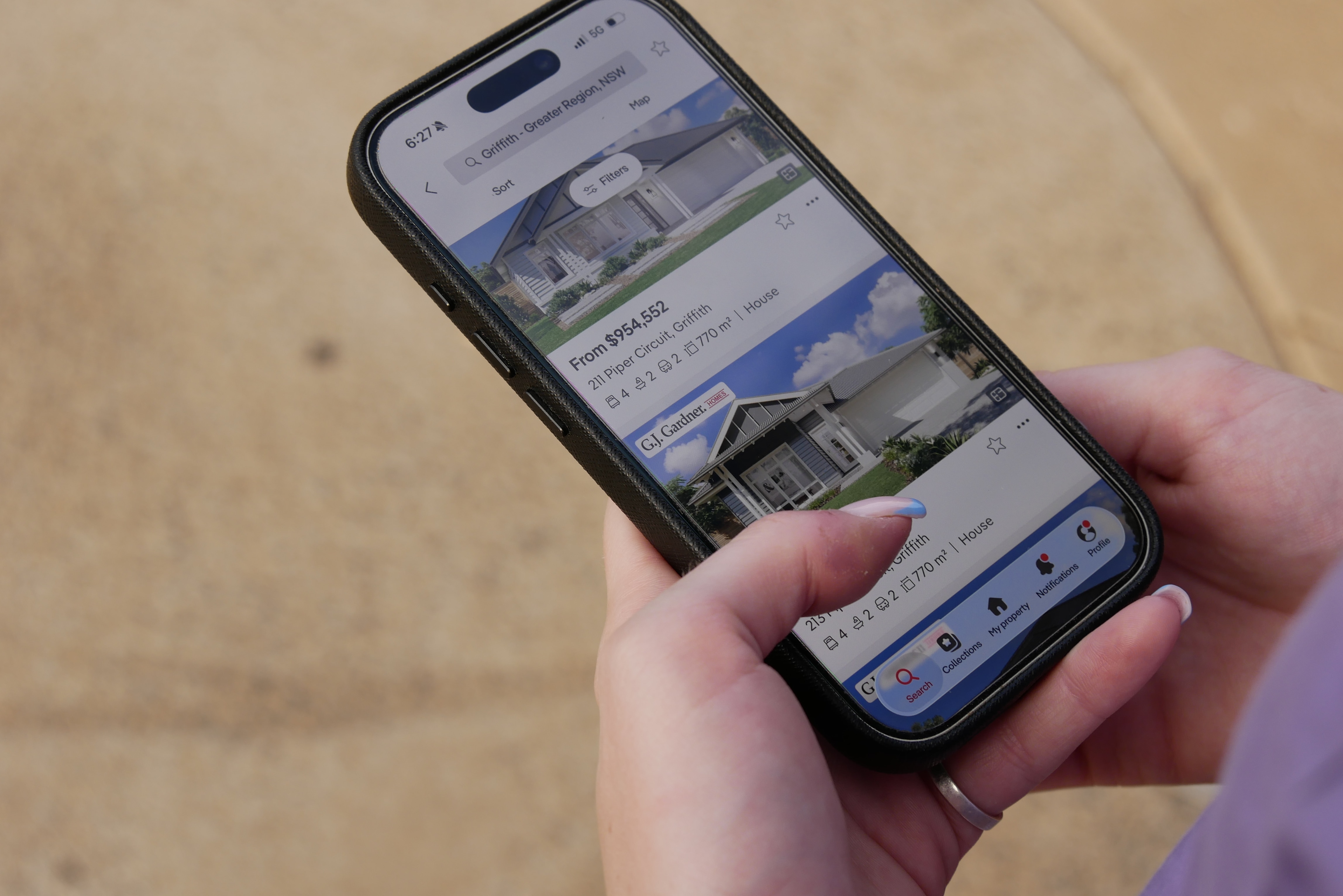 La mano de una mujer se desplaza sobre su teléfono mostrando fotografías y precios de casas.