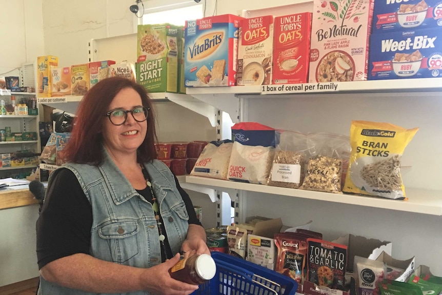 A woman stands next to shelves filled with groceries