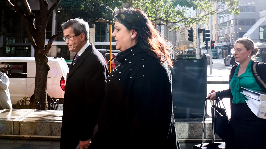 Ms Fewster walks into the building, flanked by a man and woman wearing formal clothes.