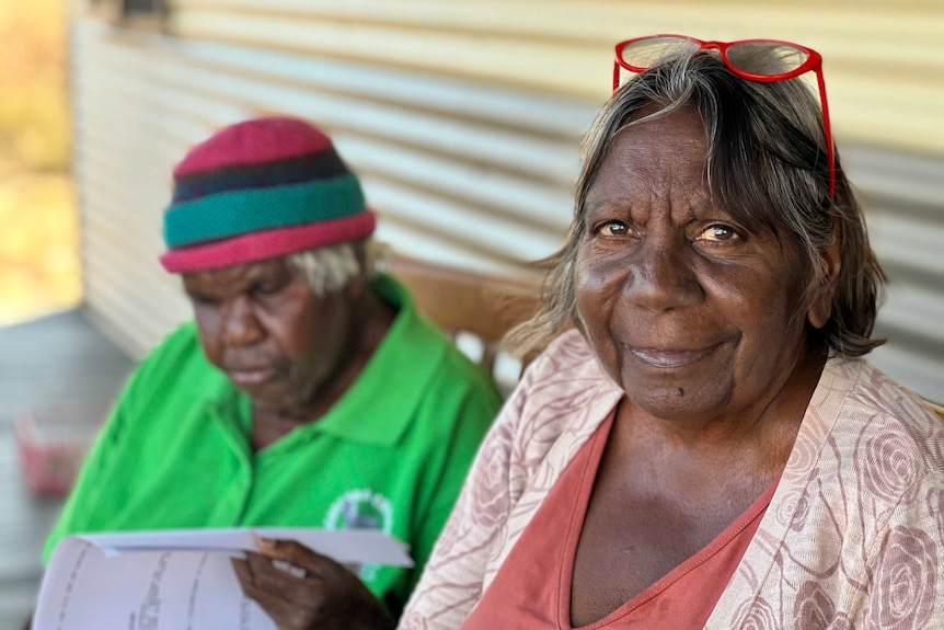 Two Aboriginal women sitting down, one smiling towards the camera, the other reading. 