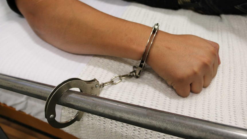 A patient is handcuffed to a hospital bed.