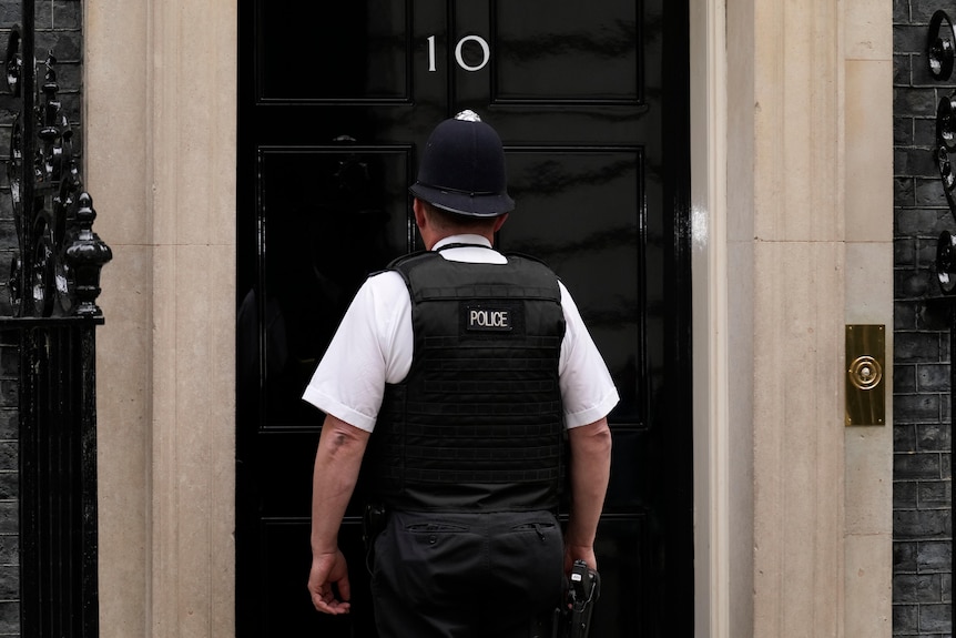 A uniformed police officer stands in front of the closed door bearing the number 10.