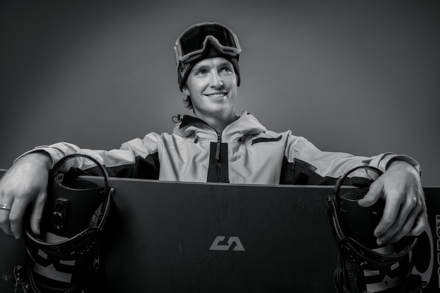 Black and white image of Scotty James holding a snowboard.