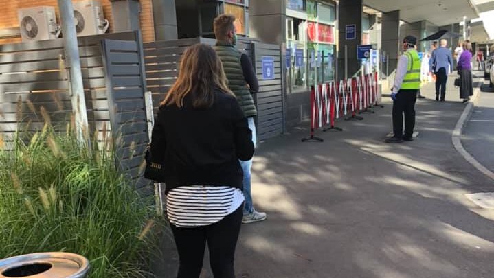 Several people stand in a queue some distance away from each other outside the Alfred Hospital.
