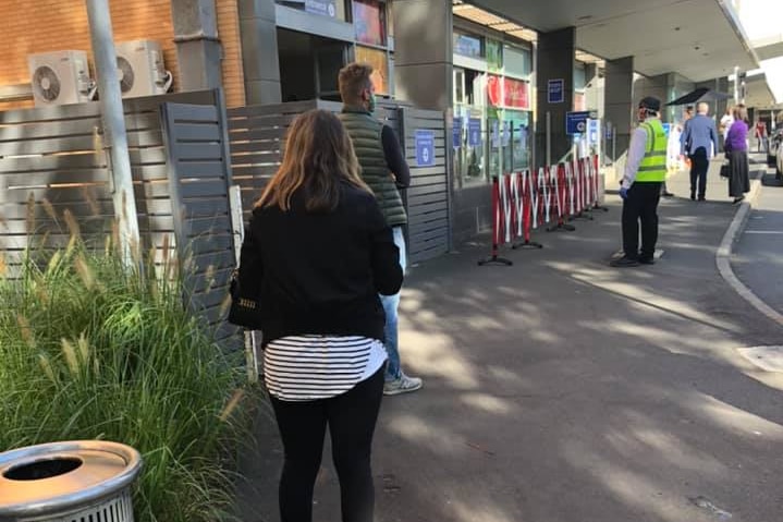 Several people stand in a queue some distance away from each other outside the Alfred Hospital.