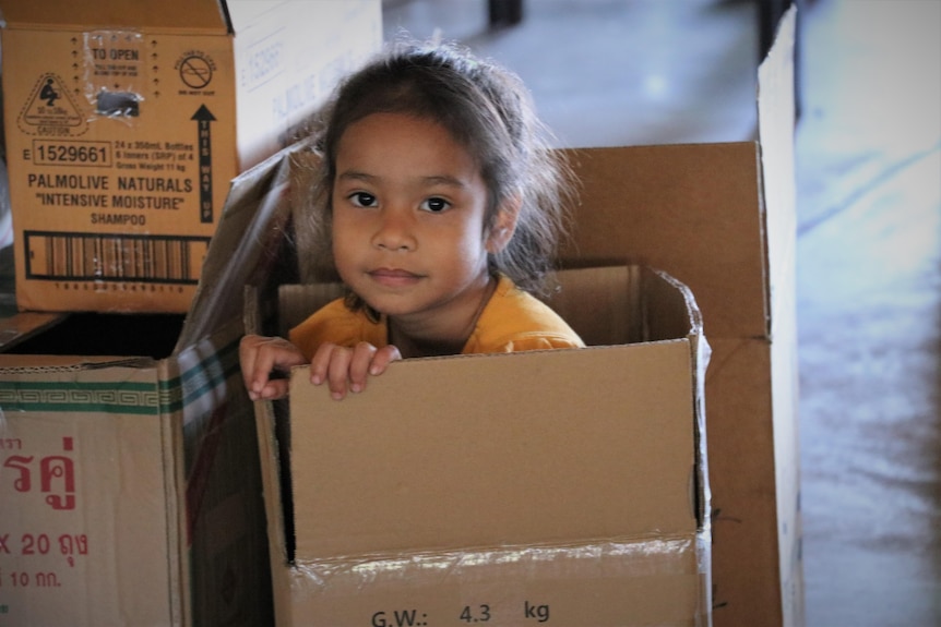 A child sits in a box during packing of donations for Timor-Leste