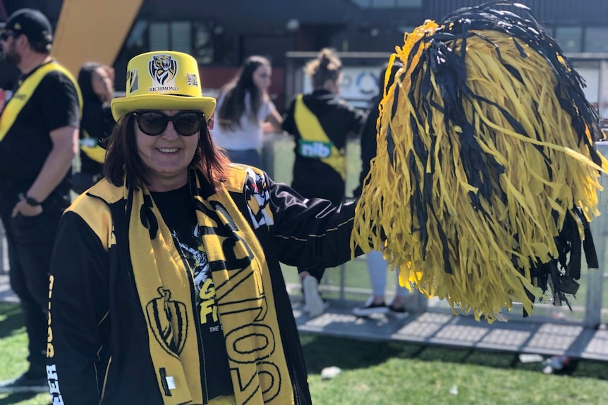 A Richmond supporter in a hat and scarf holds up a big black and yellow pom pom.