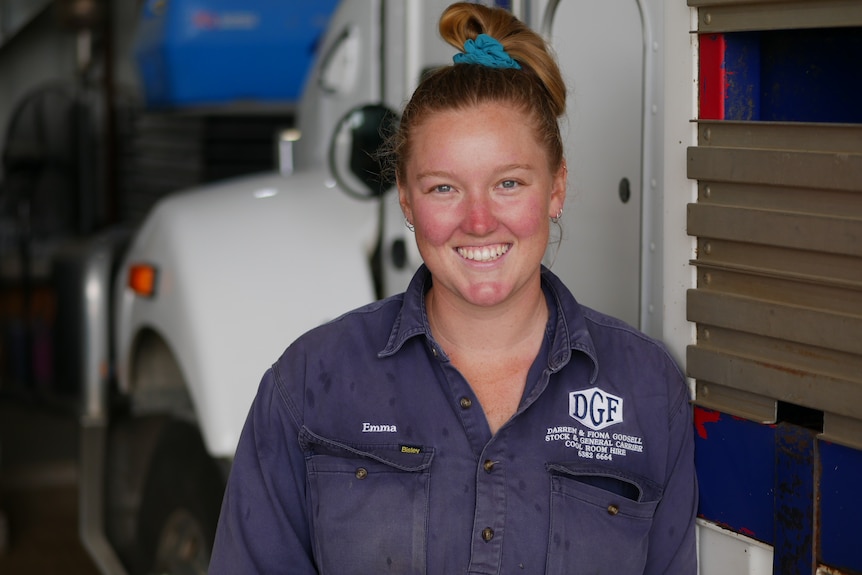 A woman in a blue shirt smiles at the camera while standing in front of a truck