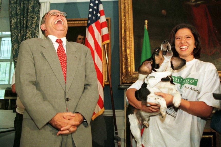 Rudy Giuliani laughing next to a woman holding a barking dog