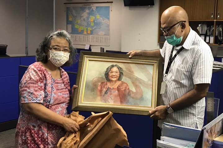 Woman and man wearing mask holding painting in an office.