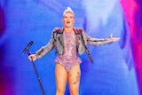 Pink stands on stage holding a mic stand as she glitters in a pink bodysuit and studded black leather jacket.