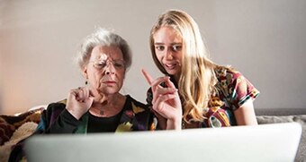 An older woman with furrowed brow and younger woman mid-speech concentrate on a computer screen.