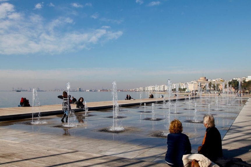 A man and woman seated by fountains on the Thessaloniki seafront.