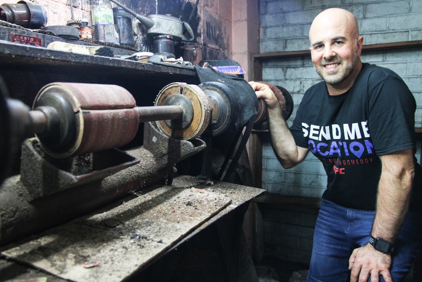 A man stands beside a finishing machine used to stitch shoes together.