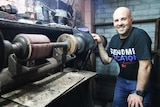 A man stands beside a finishing machine used to stitch shoes together.