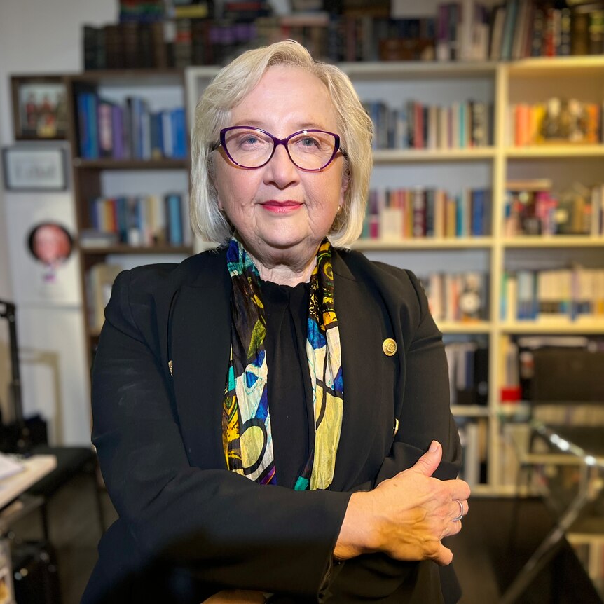 Anne Hollonds sits in an office. A glass table and a bookshelf are in the background
