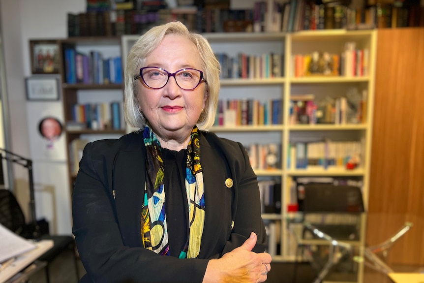 Anne Hollonds sits in an office. A glass table and a bookshelf are in the background