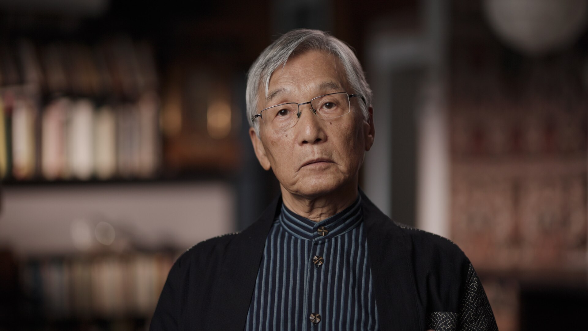 Asian man with grey hair with bookshelves behind him