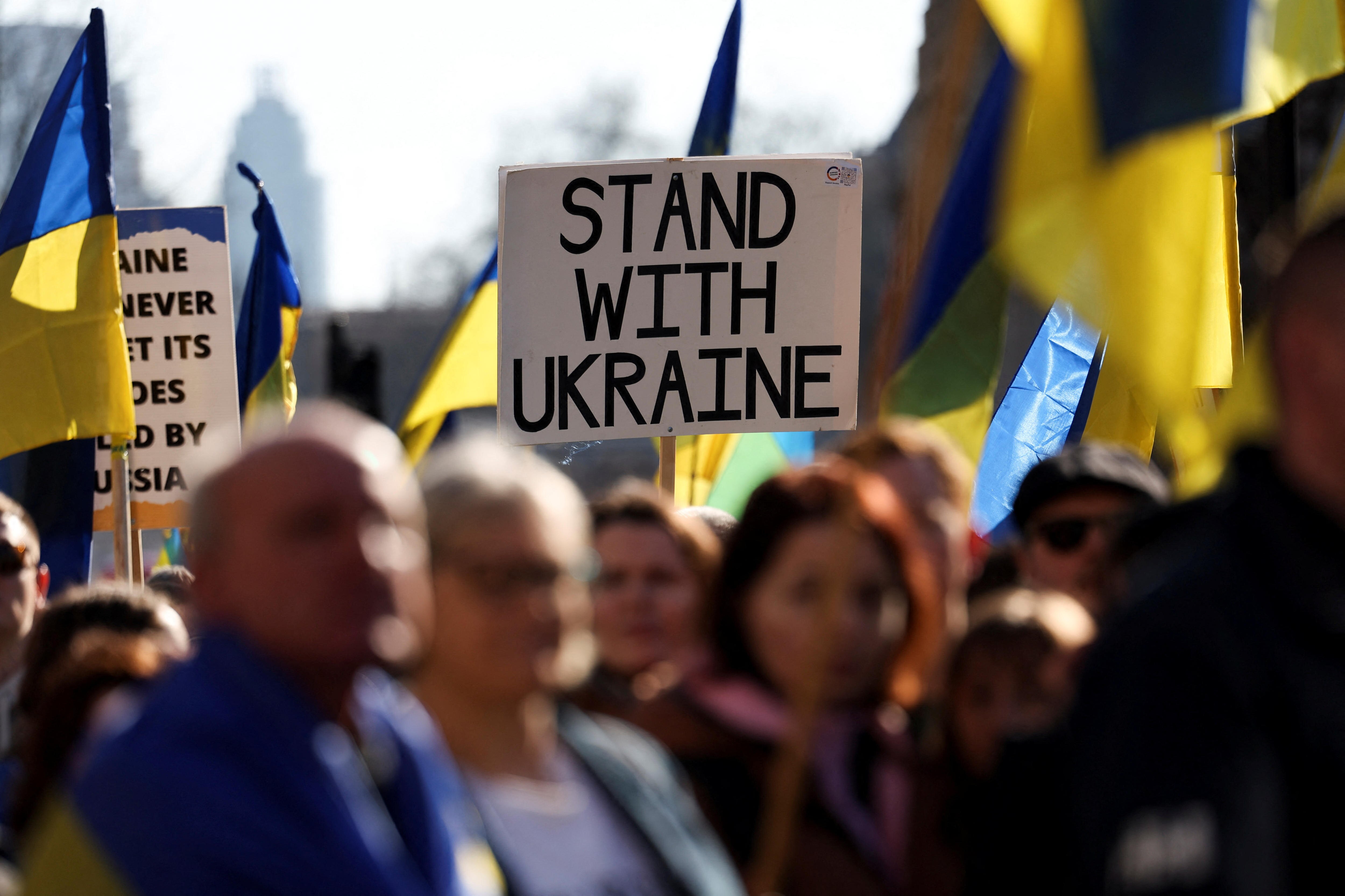 A placard reading 'Stand with Ukraine' held among Ukrainian flags in a crowd in London.