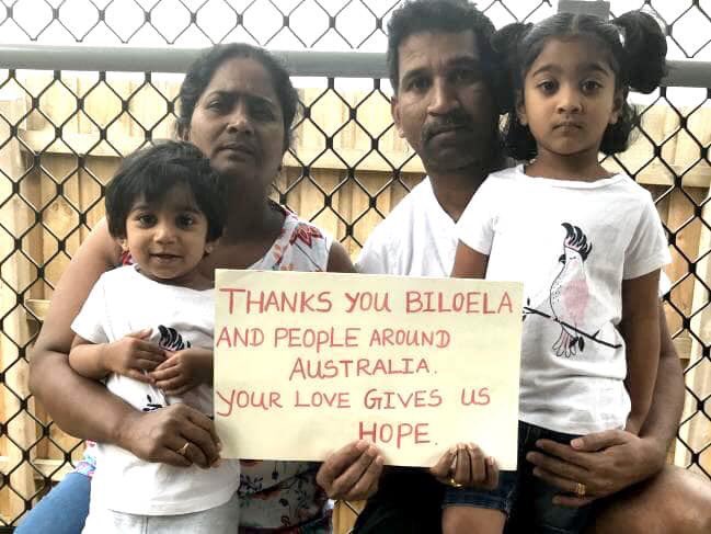 一家人靠着栅栏坐着，举着一块牌子，上面写着：“谢谢比洛埃拉和澳大利亚各地的人们。你给了我们希望”。 class=