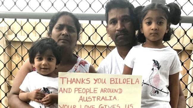 Family sit against a fence holding a sign that reads: "Thanks you Biloela and people around Australia. You give us hope".