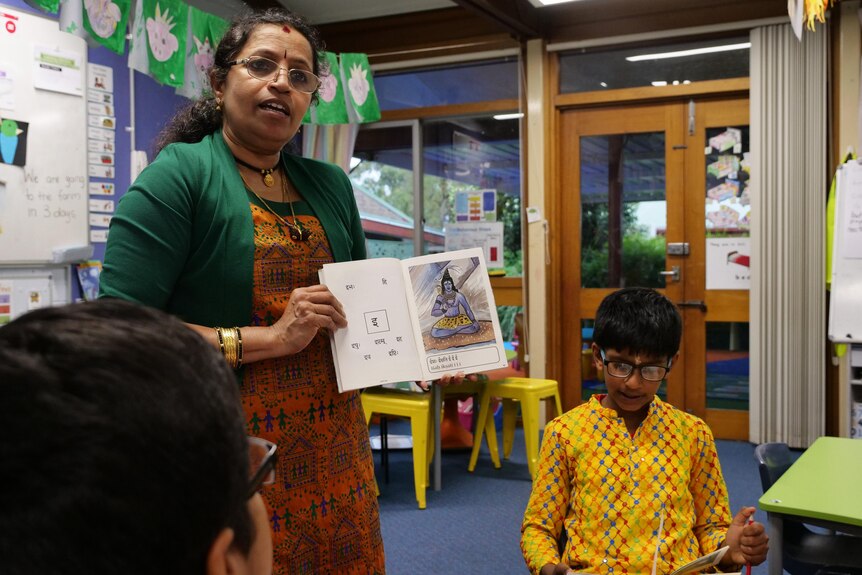 A woman shows an open book with an Indian god in a classroom