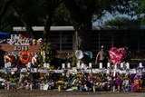 White crosses and many flowers surround the school sign at Robb Elementary after a massacre, police in background