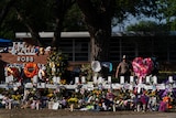 White crosses and many flowers surround the school sign at Robb Elementary after a massacre, police in background