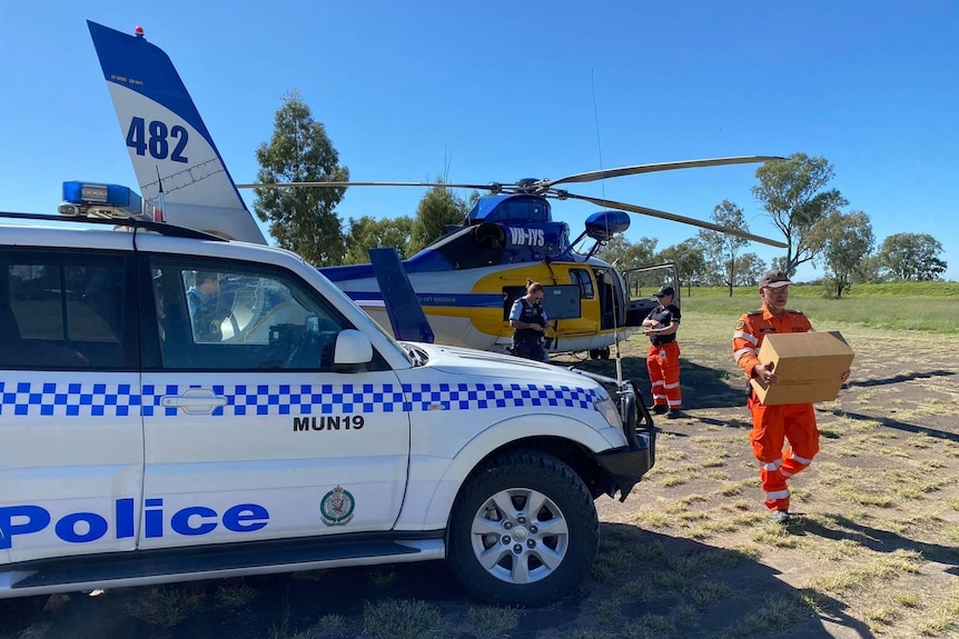 Men in high-vis gear carry boxes from a helicopter past a parked police car. 