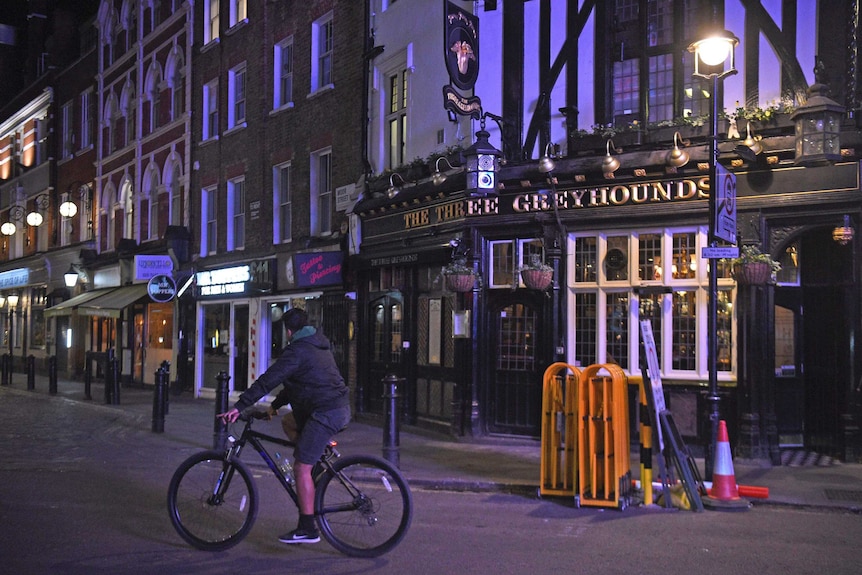 A man on a bike riding down an empty London street at night