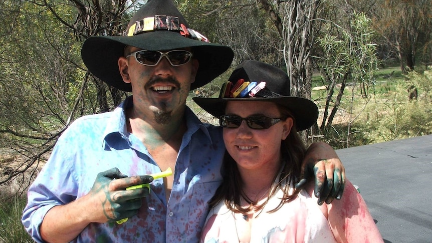 Man and woman stand arm in arm wearing cowboy hats