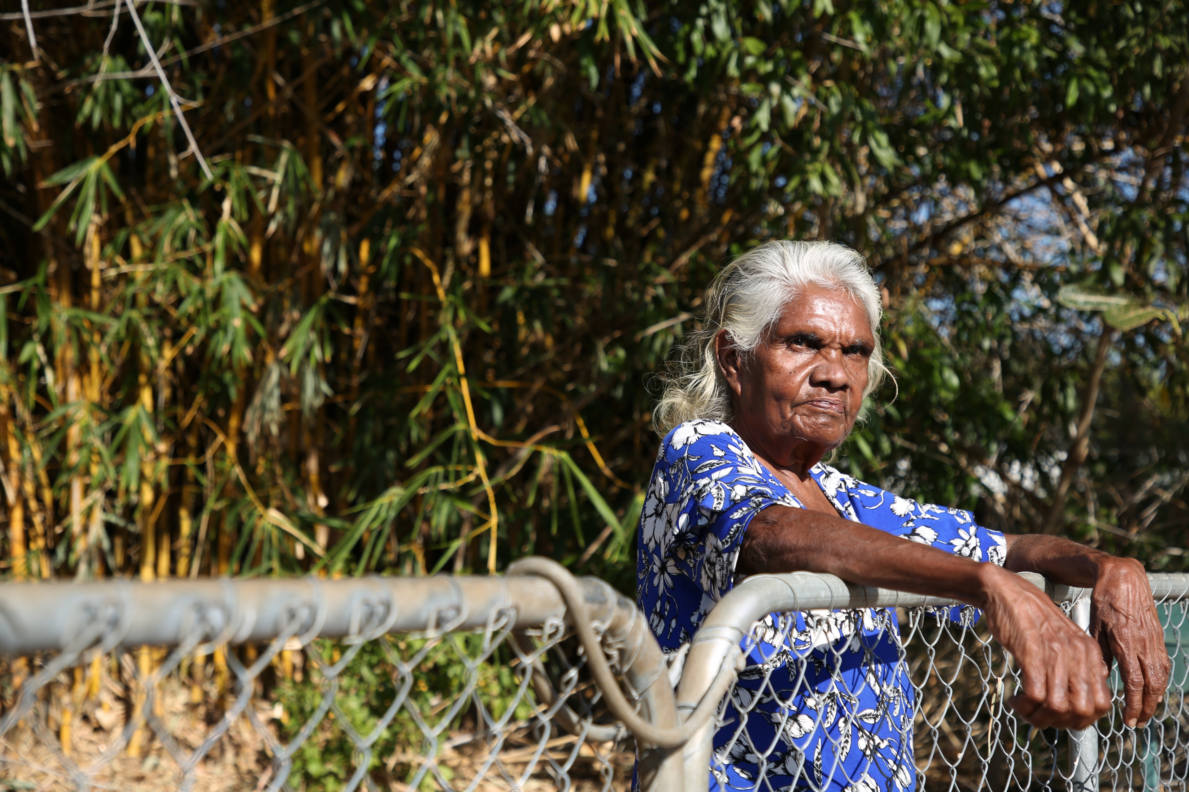 Indigenous woman Helen Fejo-Frith leans against a fence in the front yard of her home.