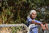 Indigenous woman Helen Fejo-Frith leans against a fence in the front yard of her home.