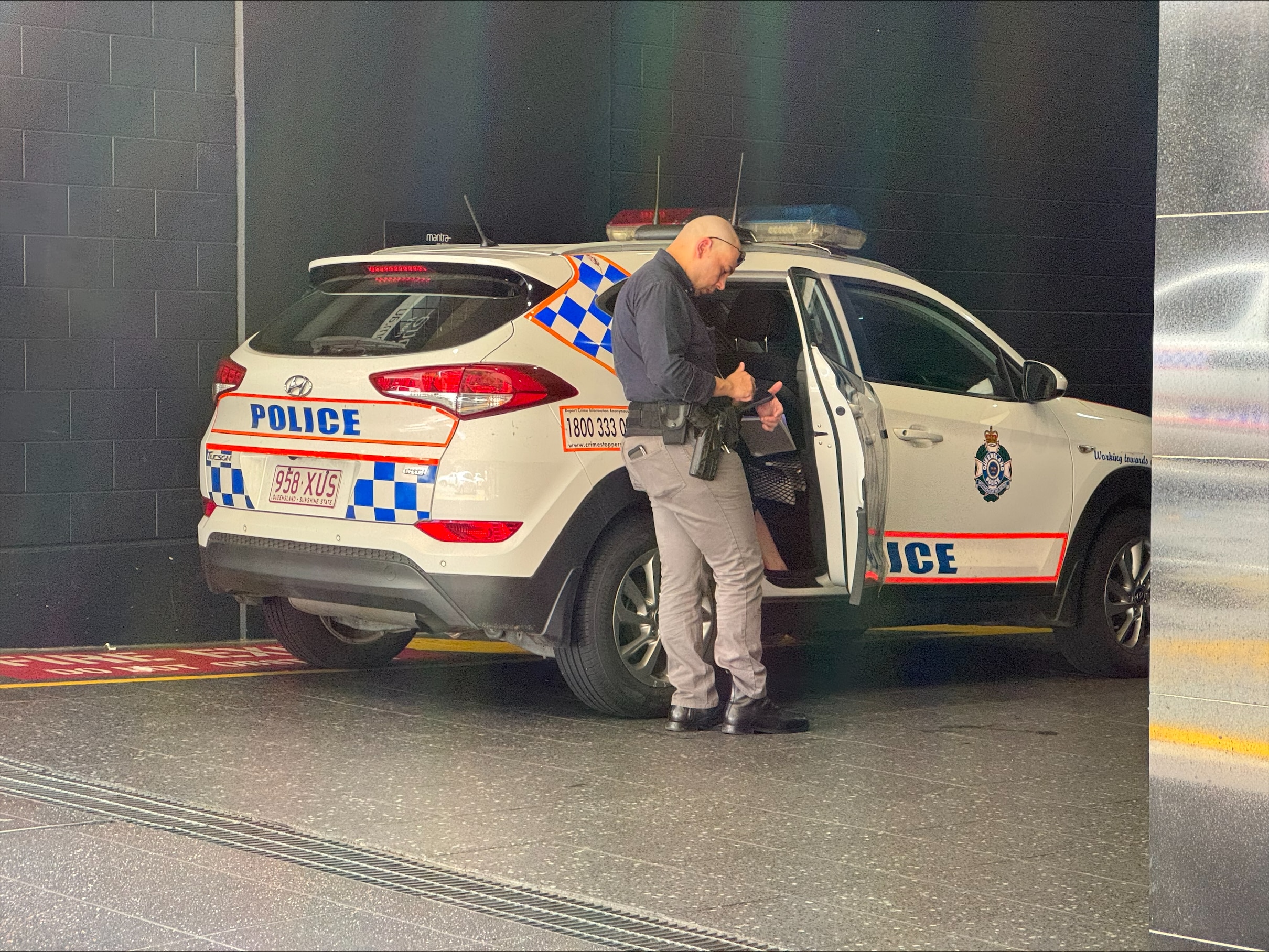 a plain clothes police officer standing at the back door of a marked police 4wd writing notes 