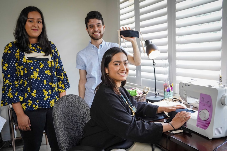 Anika Yesmin, Monish Puri pose with tailored masks, while Ayesha Barmare sits at her sewing machine.