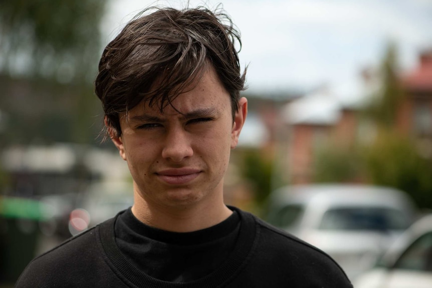 Close up of a teenage boy with dark, floppy hair looking at the camera