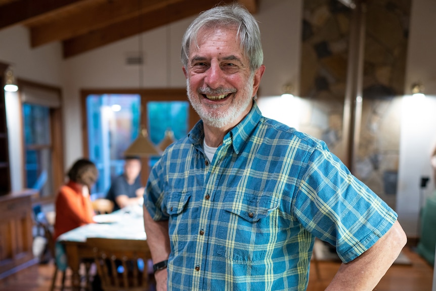 A man standing in a living room smiling with his hands on his hips.