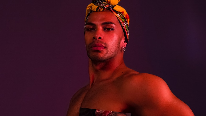 Thomas Fonua poses for the camera. He's wearing a headscarf and a photo of a woman is stuck to his chest.